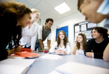 A group of high school students gathered at a table in a circle, doing a language game together