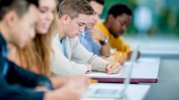 High school students take notes on paper and laptops in class