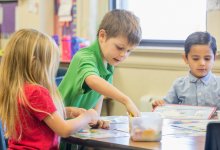 three children working at a desk with hands-on materials